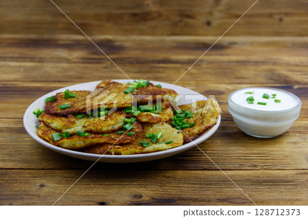 Potato pancakes with sour cream on a wooden table Potato pancakes with sour cream on a wooden table 128712373