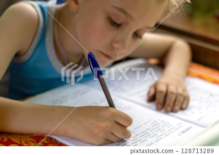 Schoolboy concentrates on doing his homework during vacation on summer cottage terrace 128713289