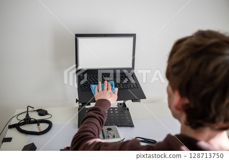 Person cleaning laptop screen with microfiber cloth on adjustable desk stand in home office Person cleaning laptop screen with microfiber cloth on adjustable desk stand in home office 128713750
