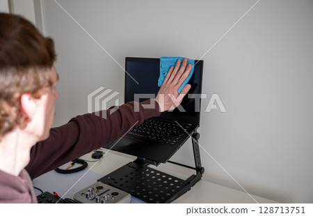Person cleaning laptop screen with microfiber cloth on adjustable desk stand in home office Person cleaning laptop screen with microfiber cloth on adjustable desk stand in home office 128713751