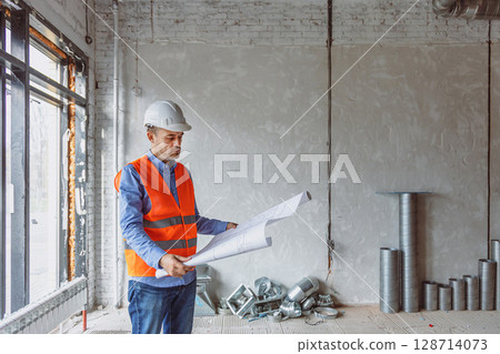 Construction worker analyzes blueprints in a newly built office space during daylight hours Construction worker analyzes blueprints in a newly built office space during daylight hours 128714073