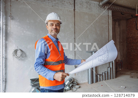 Construction manager reviewing blueprints in a renovation site with exposed brick walls and metal ducts 128714079