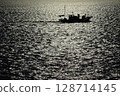 The silhouette of a fishing boat sailing on the sparkling sea in the setting sun 128714145