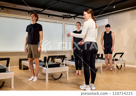 A pilates instructor guiding a group class in a modern fitness studio A pilates instructor guiding a group class in a modern fitness studio 128714225
