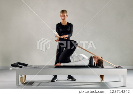 Professional Pilates session with an instructor assisting a client on a reformer 128714242