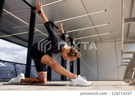 Athletic woman performing a dynamic stretch in a modern indoor space Athletic woman performing a dynamic stretch in a modern indoor space 128714297