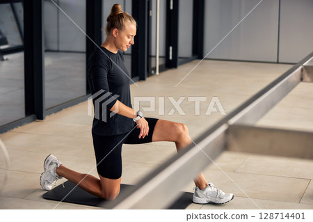 Woman Performing Stretching Exercise Indoors on Mat with Focused Expression 128714401