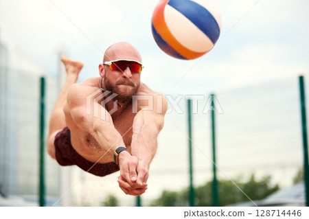 Man Diving to Hit Volleyball During Game on a Bright Sunny Day 128714446