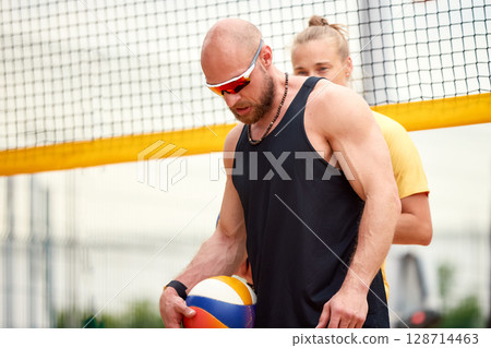 Man in sportswear holding volleyball near net during outdoor game 128714463