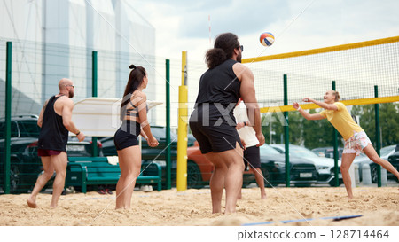 Group of friends playing beach volleyball at an outdoor sports facility 128714464