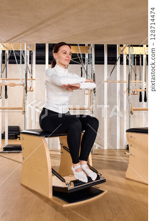 Woman practicing pilates exercise on reformer chair in modern fitness studio Woman practicing pilates exercise on reformer chair in modern fitness studio 128714474