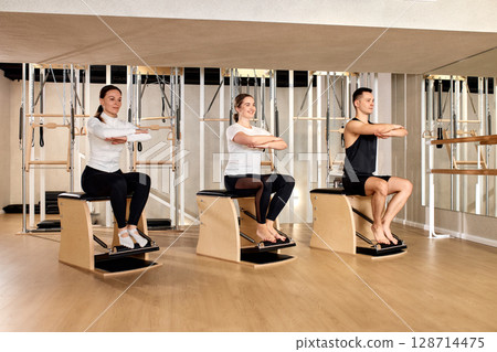Group fitness class using pilates chairs in a modern studio Group fitness class using pilates chairs in a modern studio 128714475