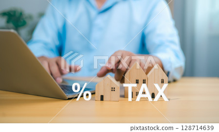 Tax property planning with a businessman using a laptop and wooden house models to represent real estate investment and financial calculation. 128714639