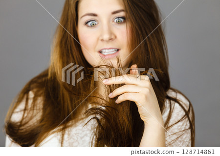 Worried woman looking at her dry hair ends Worried woman looking at her dry hair ends 128714861