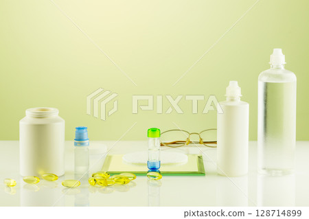Ophthalmology concept with containers with contact lenses, eye drops, clean solutions, vitamins and eyeglasses. Night contact lenses. Advertising contact lenses for vision. Optical store and eye care Ophthalmology concept with containers with contact lenses, eye drops, clean solutions, vitamins and eyeglasses. Night contact lenses. Advertising contact lenses for vision. Optical store and eye care 128714899