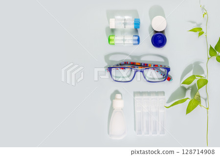 Ophthalmology concept with kid eyeglasses, containers with contact lenses and moisturizing eye drops on blue background with copy space. Concept of eyecare, eye treatment and good vision. Flat lay Ophthalmology concept with kid eyeglasses, containers with contact lenses and moisturizing eye drops on blue background with copy space. Concept of eyecare, eye treatment and good vision. Flat lay 128714908