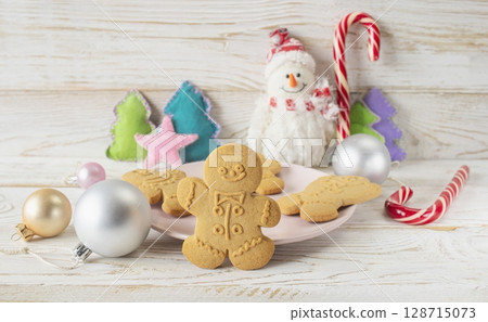 Christmas gingerbread cookies in the shape of a snowman on a white wooden background. Christmas decorations. Christmas gingerbread cookies in the shape of a snowman on a white wooden background. Christmas decorations. 128715073