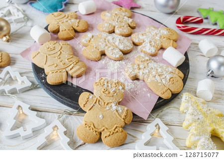Christmas gingerbread cookies in the shape of a snowman on a white wooden background. Christmas decorations. Top view, flat lay. Christmas gingerbread cookies in the shape of a snowman on a white wooden background. Christmas decorations. Top view, flat lay. 128715077