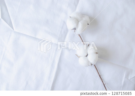 White cotton flowers on white bed linen, top view, copy space.  128715085