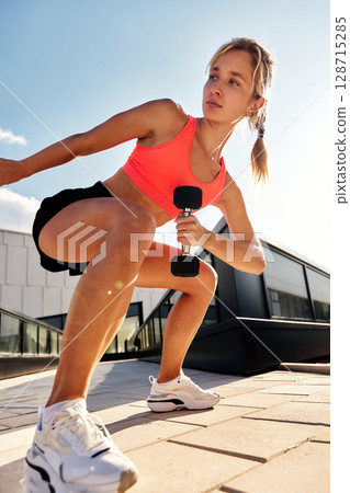 Determined athletic woman training outside with weights on a sunny day Determined athletic woman training outside with weights on a sunny day 128715285