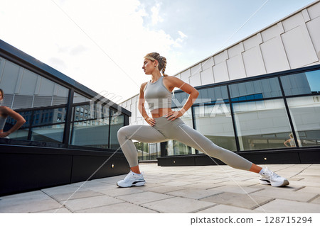 Young woman performing fitness stretching outdoors in a modern city setting Young woman performing fitness stretching outdoors in a modern city setting 128715294