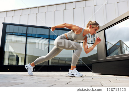 Young woman performing outdoor exercise wearing sporty attire on city rooftop terrace Young woman performing outdoor exercise wearing sporty attire on city rooftop terrace 128715323