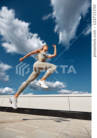 Young athlete jumping energetically against a blue sky 128715350