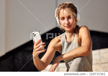 Active woman with headphones using smartphone during outdoor fitness break 128715361