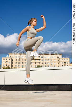 Young woman performing a fitness jump exercise outdoors in daytime 128715388