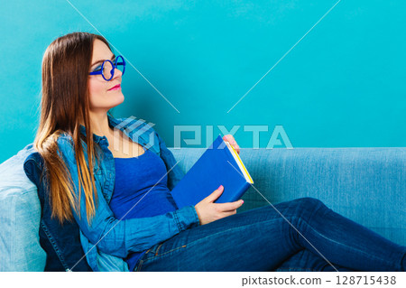 Woman sitting on couch reading book at home Woman sitting on couch reading book at home 128715438