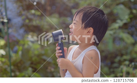 5-year-old boy using a handheld fan 128715706