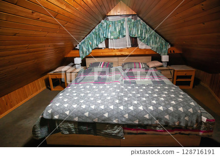 Wooden bed in attic in mountain hut. Rustic bedroom with sleeping double bed 128716191