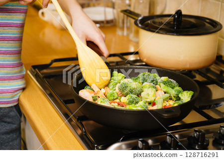 Girl frying vegetables on pan Girl frying vegetables on pan 128716291