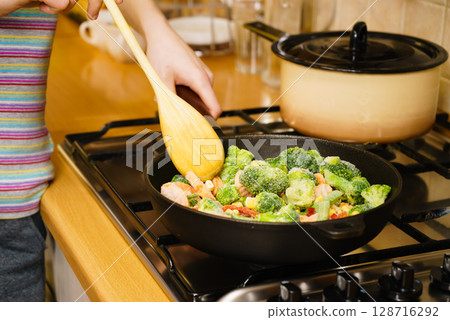 Girl frying vegetables on pan Girl frying vegetables on pan 128716292