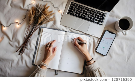 Stylish Workspace with Laptop, Planner, Coffee, Phone, and Dried Flowers on Soft Blanket Surface 128716390