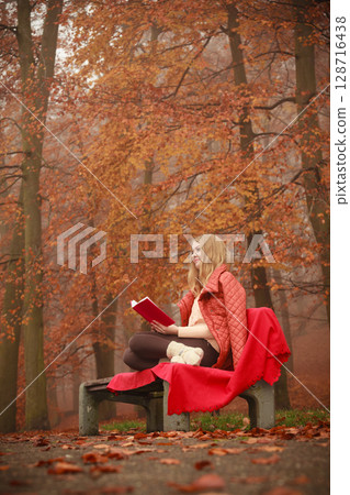 Blonde girl reading book in autumn scenery 128716438