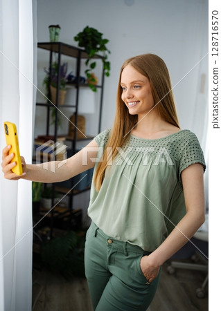 Smiling woman takes a selfie in a cozy indoor setting with plants 128716570