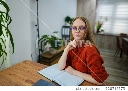 Thoughtful young woman seated in a cozy workspace at home 128716575