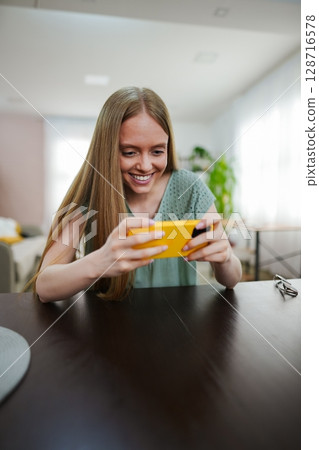 Joyful moment of a young woman engaging with a phone in a bright space 128716578