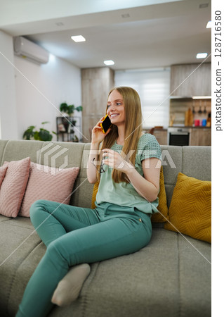 Woman enjoying a relaxing phone call in a cozy living room 128716580