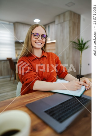 Focused young woman jotting down ideas in a cozy workspace 128716582