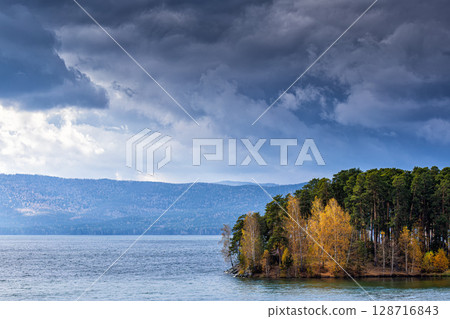 A small forested island on a picturesque lake on a cloudy autumn day 128716843