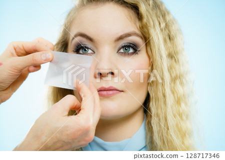 Woman using oil blotting tissues on model 128717346