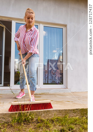 Woman cleaning patio using brush broom 128717437