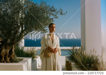 A woman wearing a white dress stands in front of a tree 128717728