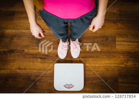 Woman with pink sneakers on bathroom weight scale Woman with pink sneakers on bathroom weight scale 128717854