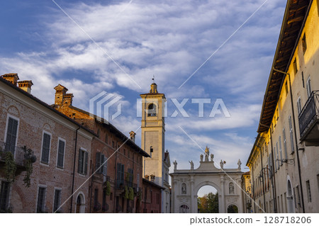Cherasco, Italy, bell tower and Arco del Belvedere standing tall under blue sky Cherasco, Italy, bell tower and Arco del Belvedere standing tall under blue sky 128718206