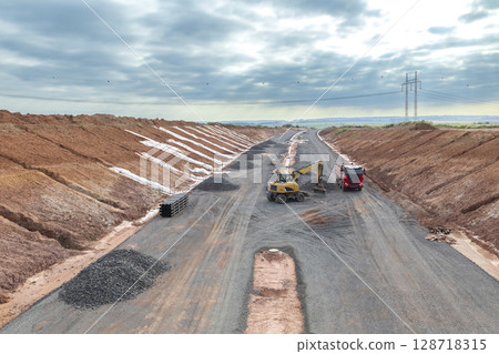 Wheel loader loading gravel into dump truck during highway construction in Czechia 128718315