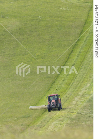 Tractor Mowing Grass on a Rolling Hill in Slovakia Tractor Mowing Grass on a Rolling Hill in Slovakia 128718464
