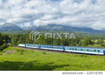 Passenger train passing through green valley and forest in High Tatras, Slovakia Passenger train passing through green valley and forest in High Tatras, Slovakia 128718789